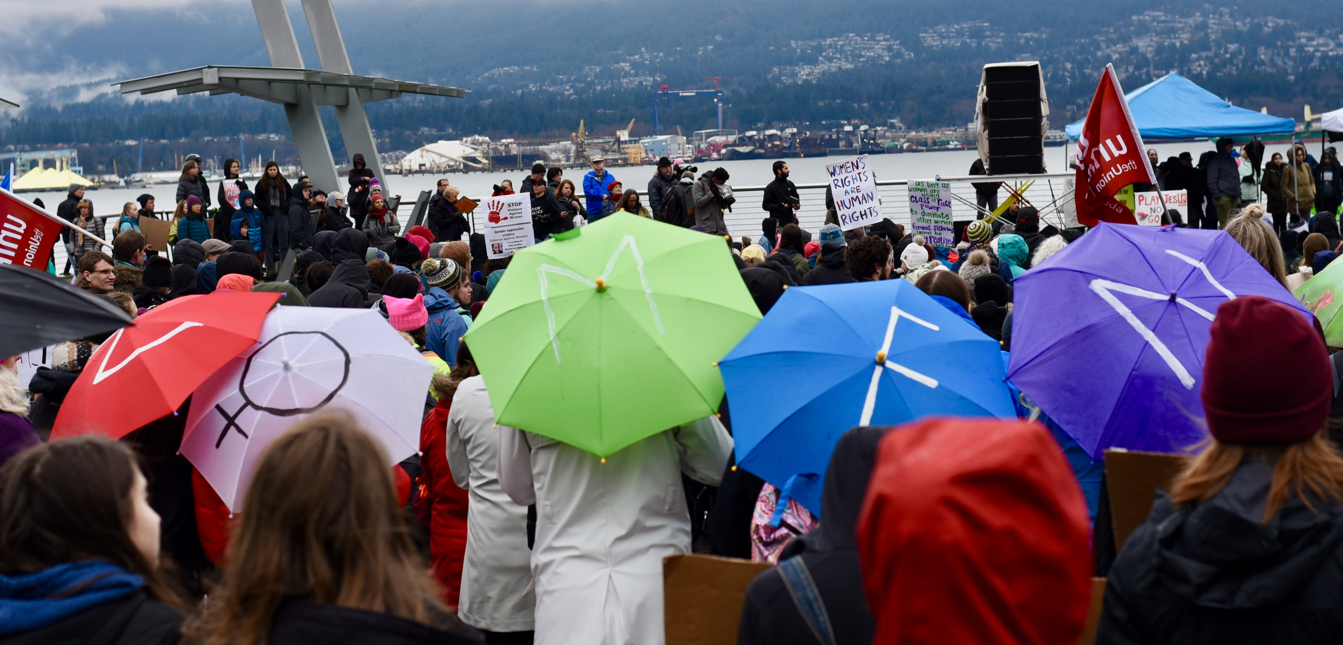 Demonstrators at Jack Poole plaza spell out "WOMEN" with their umbrellas.